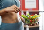 Effective Ways To Keep Your Stomach Healthy Close up of a sport woman with her sexy belly, she holding a bowl of fresh healthy food