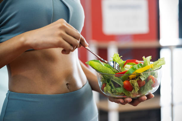 Effective Ways To Keep Your Stomach Healthy Close up of a sport woman with her sexy belly, she holding a bowl of fresh healthy food